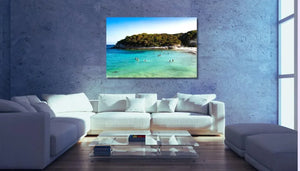 Tableau mural représentant une crique aux eaux turquoise avec baigneurs, plage claire et végétation naturelle sous un ciel lumineux