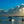 Child standing in shallow water at sunset with boats and dramatic clouds over the sea