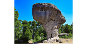 Tableau décoratif représentant une roche monumentale sculptée par le temps au cœur d’une forêt de pins sous un ciel bleu