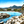 Isula Rossa - Tableau décoratif représentant une baie méditerranéenne aux eaux turquoise, bordée de rochers, de palmiers et de montagnes sous un ciel bleu lumineux. Plexiglas - ESPOIR PHOTOS