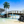 Tranquil beach scene with wooden bridge over water, palm trees, and blue sky