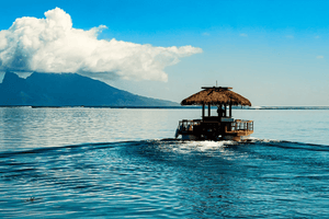 Tropical boat with thatched roof on blue ocean, distant island and clouds, serene landscape