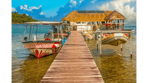 Wooden dock with boats and a thatched-roof hut over clear tropical water