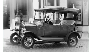Monochrome photo of a vintage classic car with soft top parked on city street
