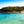 Tableau mural représentant une crique aux eaux turquoise avec baigneurs, plage claire et végétation naturelle sous un ciel lumineux