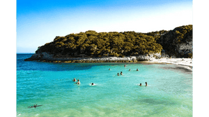 Tableau mural représentant une crique aux eaux turquoise avec baigneurs, plage claire et végétation naturelle sous un ciel lumineux
