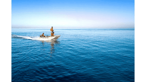 Three people on a small aluminum boat crossing calm blue ocean under clear sky