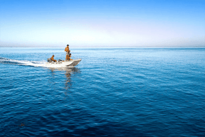 Three people riding a small boat across calm blue ocean under a clear sky.