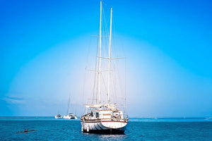 Old sailboat anchored on calm blue sea with clear sky and other boats in the distance