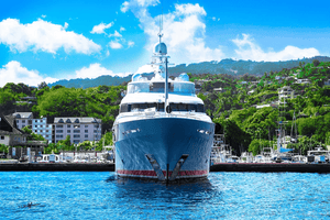 Luxury yacht docked in a marina with lush green hills and blue sky in the background