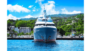 Luxury yacht docked at marina with blue sky, water, and lush green hills in background