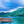 Rustic paddle boat on clear blue water with lush green island and cloudy sky in background