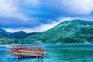 Wooden paddle boat on tranquil blue water with lush green island and cloudy sky