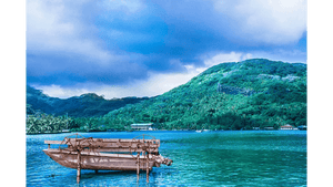 Tableau mural représentant un bateau traditionnel sur un lagon turquoise, devant une montagne tropicale verdoyante sous un ciel nuageux